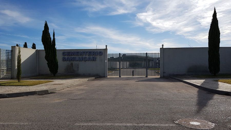 Un edificio blanco con un cartel azul está rodeado de árboles y una valla.