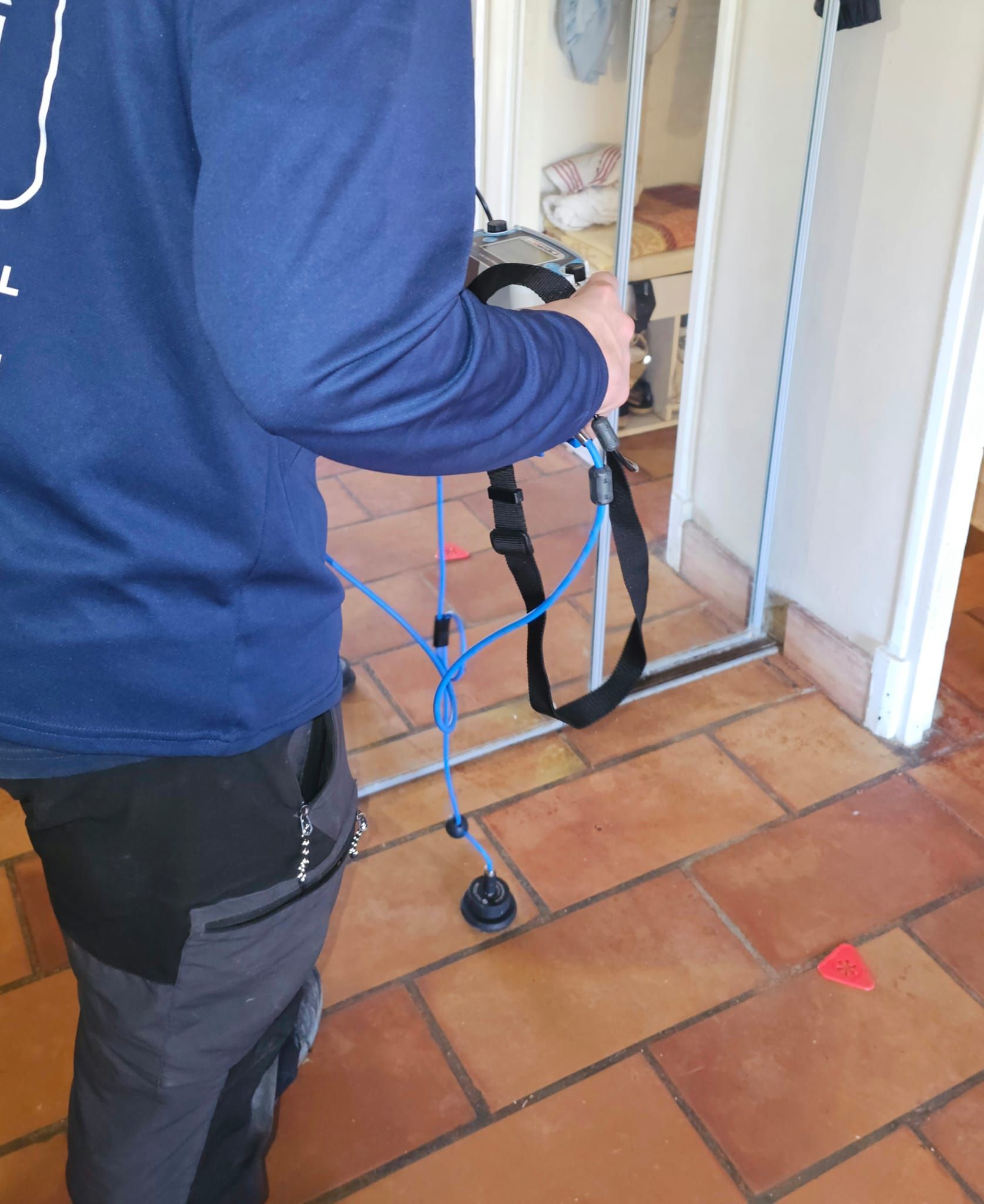 Personne tenant un outil près d'une porte ouverte, sol carrelé.