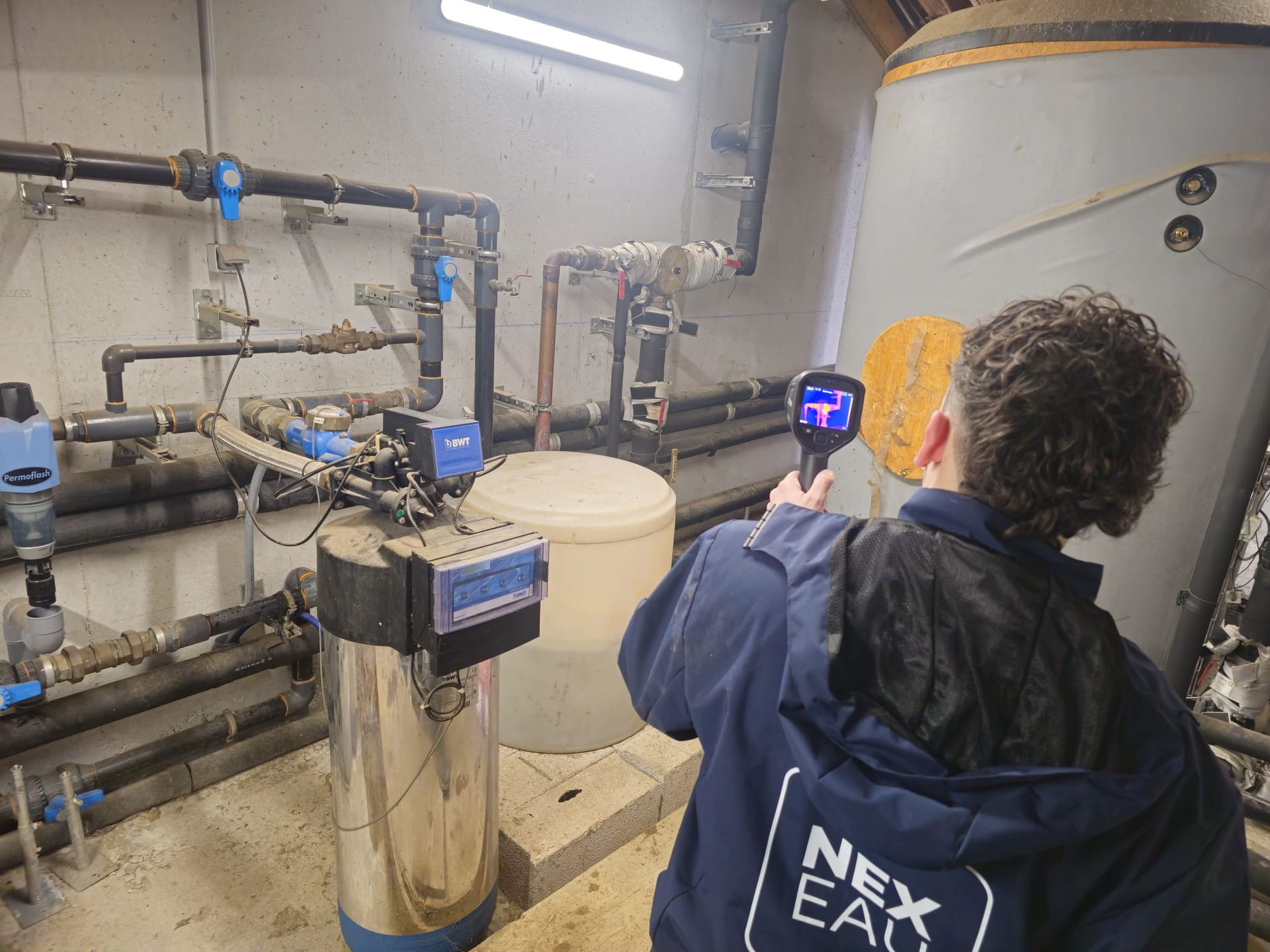 Personne utilisant une caméra thermique sur des canalisations dans un local technique. Équipement, réservoir.