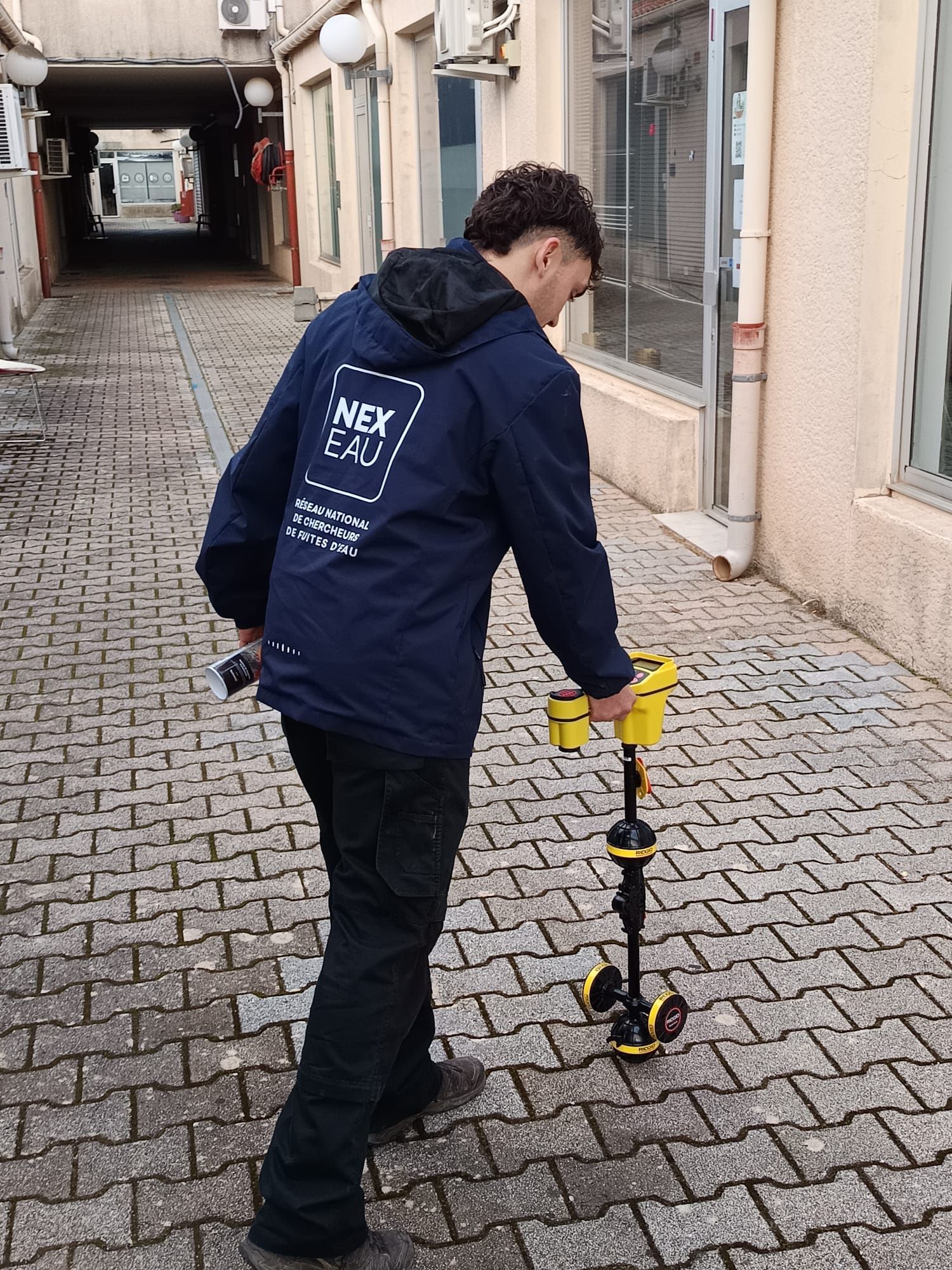Un homme en veste utilise un radar à pénétration de sol sur une allée en briques.