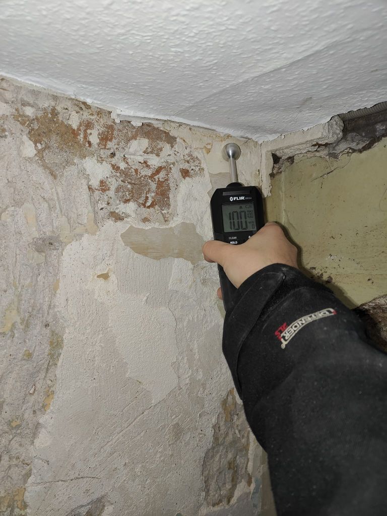 Une personne inspecte des canalisations dans un local technique à l'aide d'une caméra thermique. L'écran de la caméra affiche des variations de température.