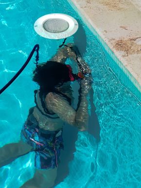 Personne sous l'eau, près du bord de la piscine, travaillant près du projecteur de la piscine.