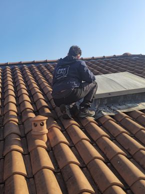 Technicien se tenant près d'un puit de lumière sur un toit tuile.