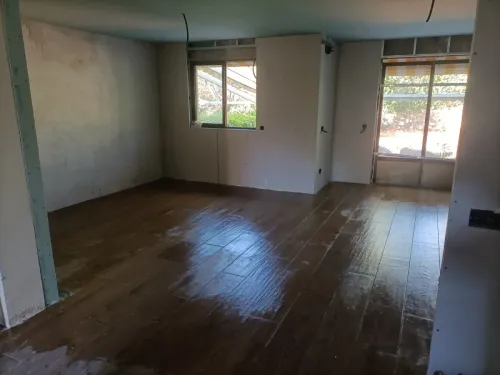 Habitación vacía con suelo de madera sin terminar, dos ventanas y cableado a la vista.