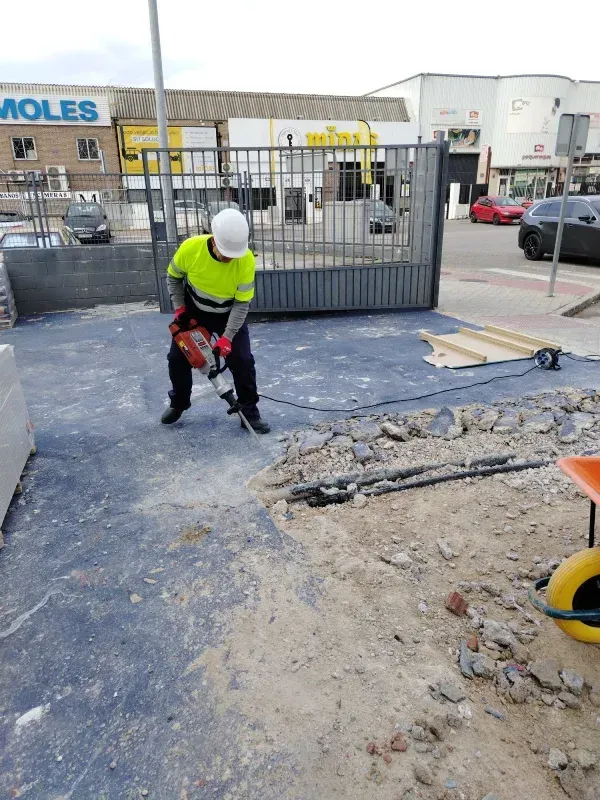 Un trabajador con chaleco de seguridad utiliza un martillo neumático sobre una superficie de hormigón