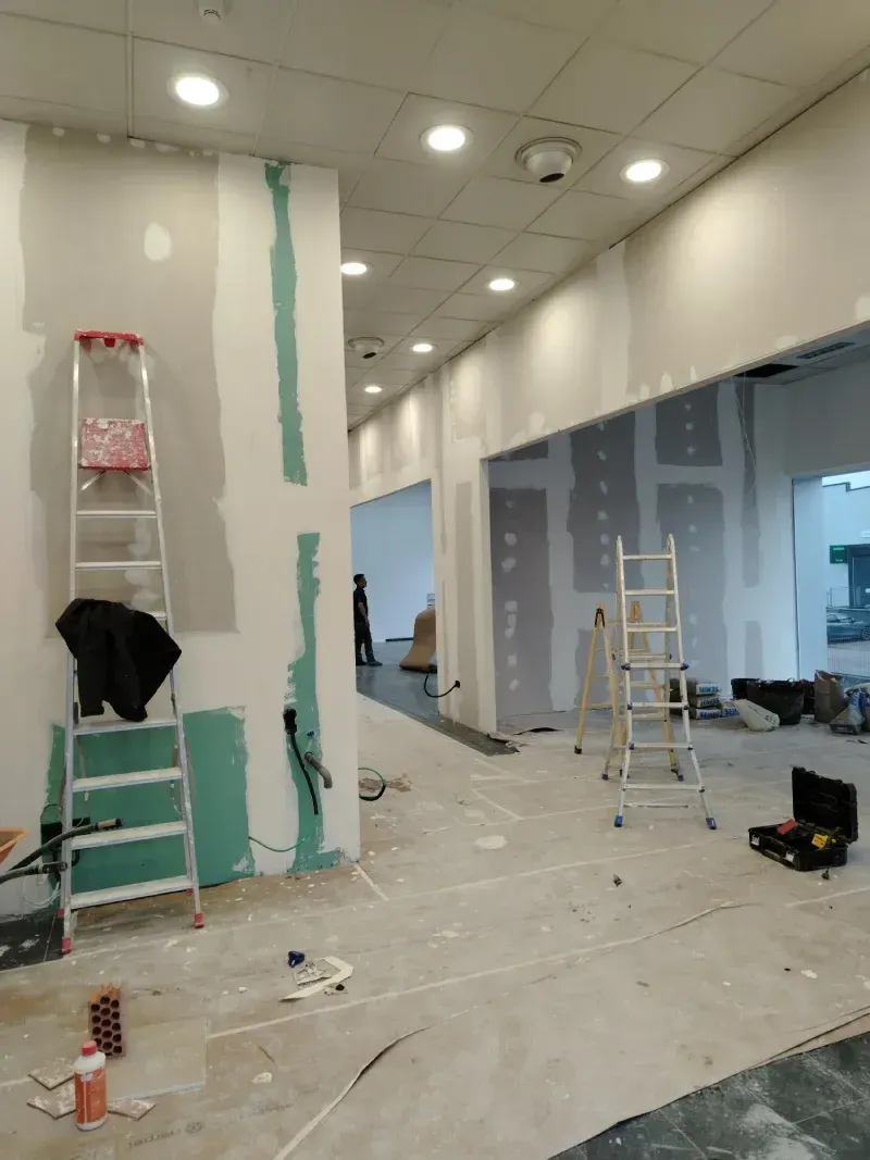 Interior en construcción con paneles de yeso y escaleras, mostrando un pasillo e iluminación empotrada.