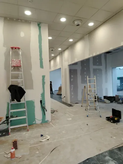 Interior en construcción con paneles de yeso y escaleras, mostrando un pasillo e iluminación empotrada.