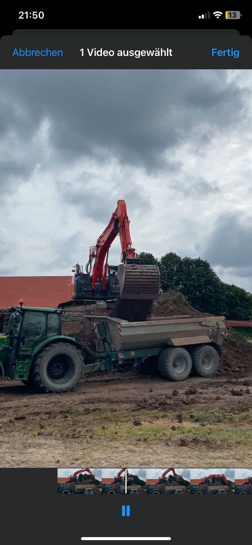 Ein roter Kran hebt Baumaterialien auf einer Baustelle mit Betonpfeilern und Fahrzeugen. Bewölkter Himmel.
