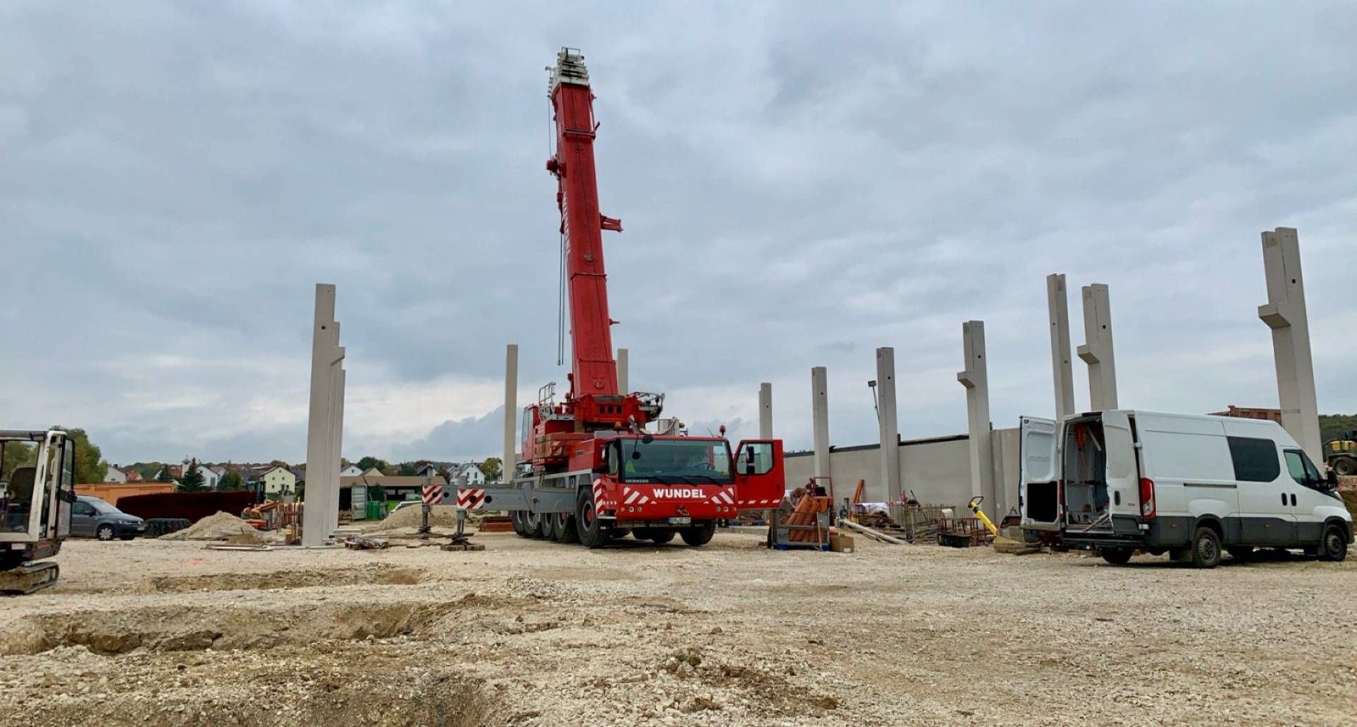 Über Steinstufen gelangt man zu einer Kiesterrasse, die von einer Steinmauer und einer grünen Hecke umgeben ist; im Hintergrund ist ein weißes Haus zu sehen.