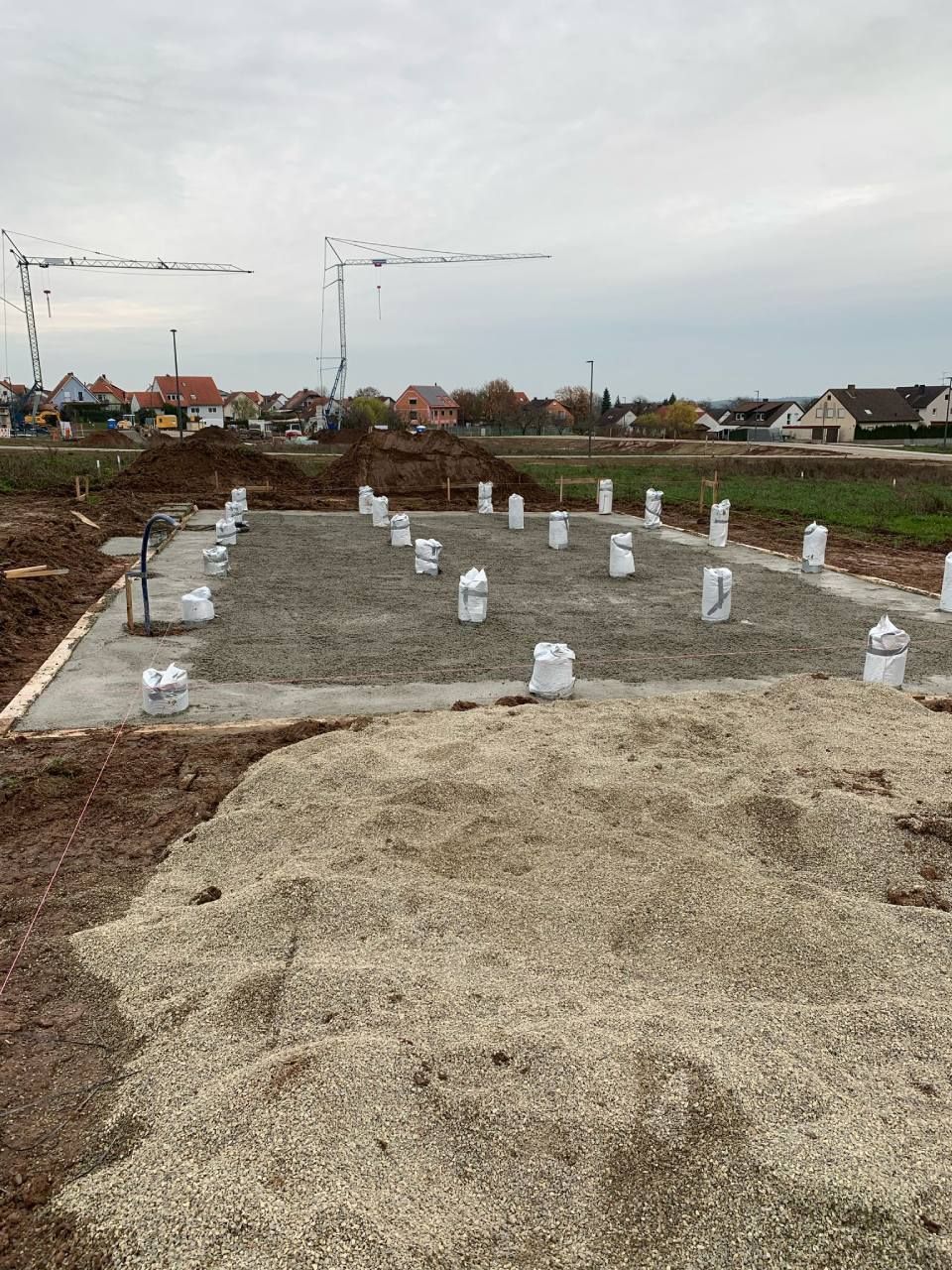 Auf einer Baustelle wird Beton mit einem Betonmischer in eine Fundamentschalung gegossen. Zwei Arbeiter sind in der Nähe. Blauer Himmel.