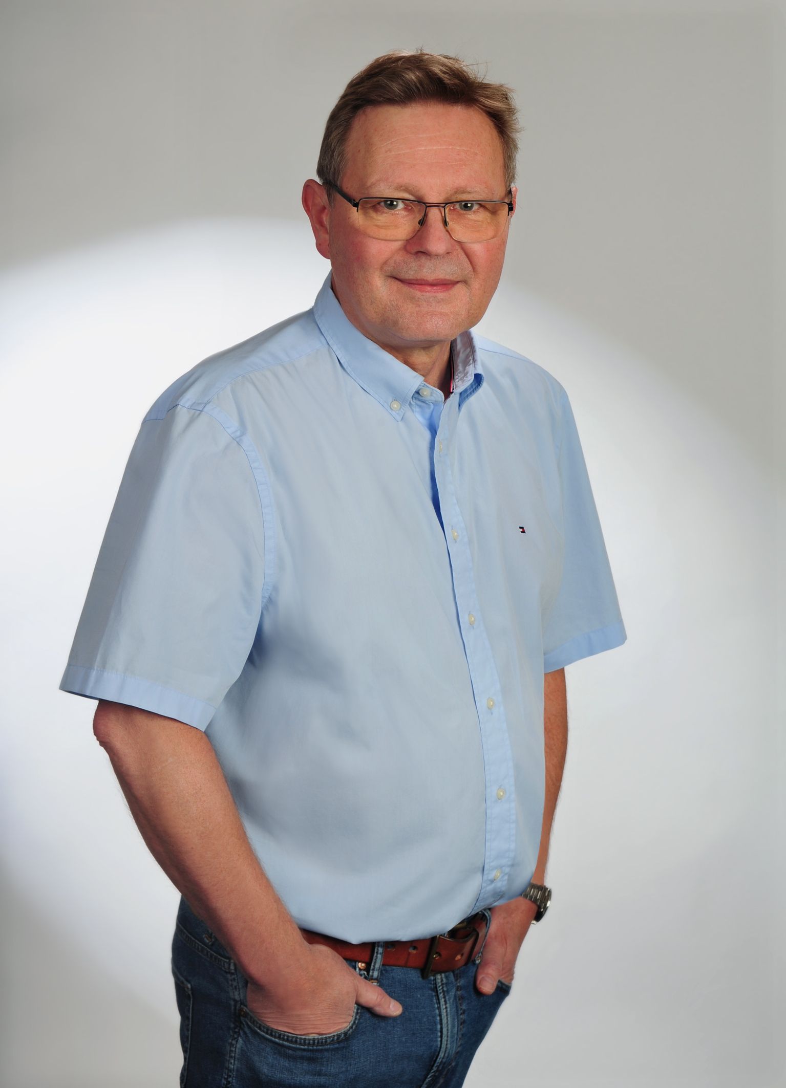 Andreas Kaschynski, mit Brille und kurzärmeligem blauem Hemd | Hände in den Taschen | lächelnd