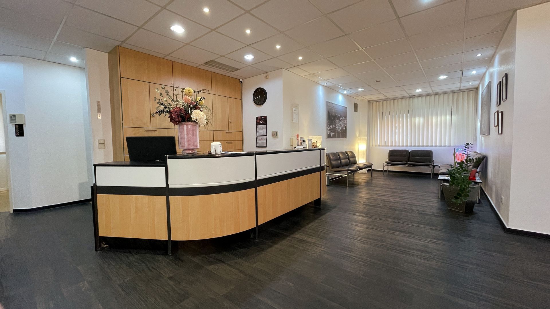 Geschwungener Empfangstresen in hellem Holz | Sitzgelegenheiten mit brauner Lederoptik | Dunkler Holzboden