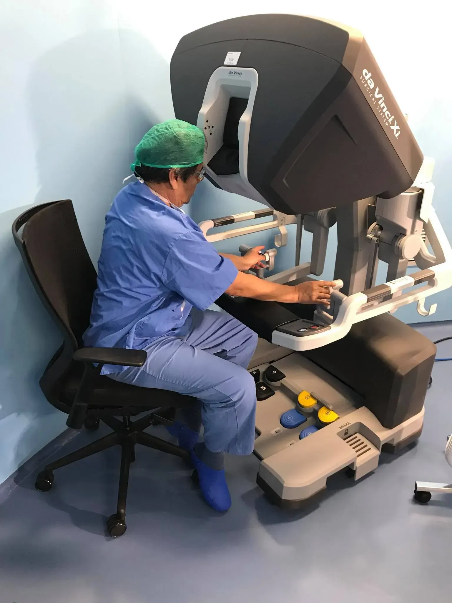 Un cirujano sentado en la consola de un robot quirúrgico da Vinci, manejando los controles con las manos.