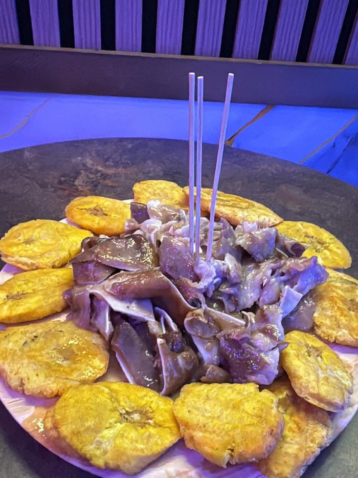 Un plato de orejas de cerdo en rodajas con tres palillos, dispuestas en círculo con varios tostones
