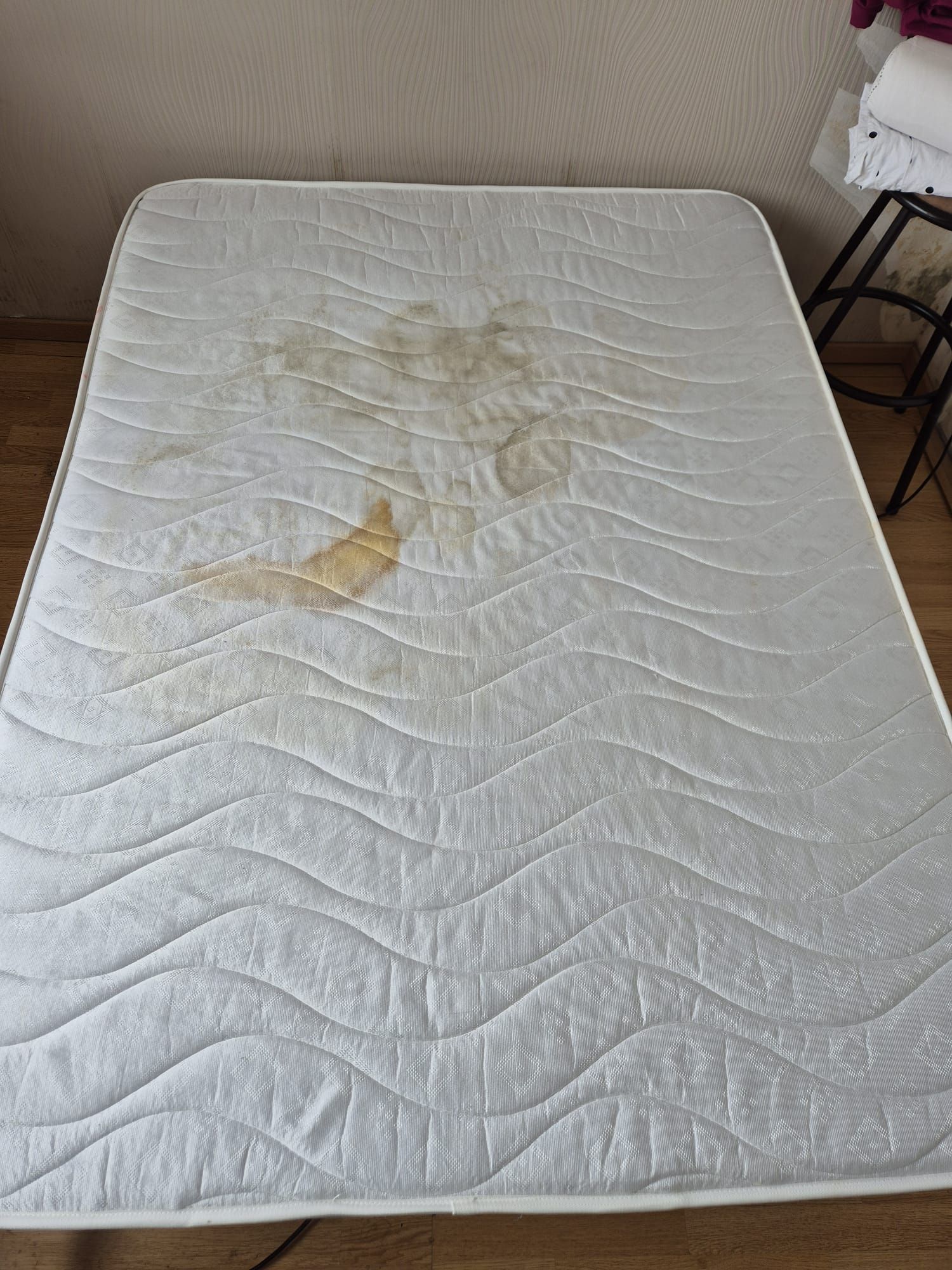 Matelas blanc taché de taches jaunes/brunes sur un plancher en bois.