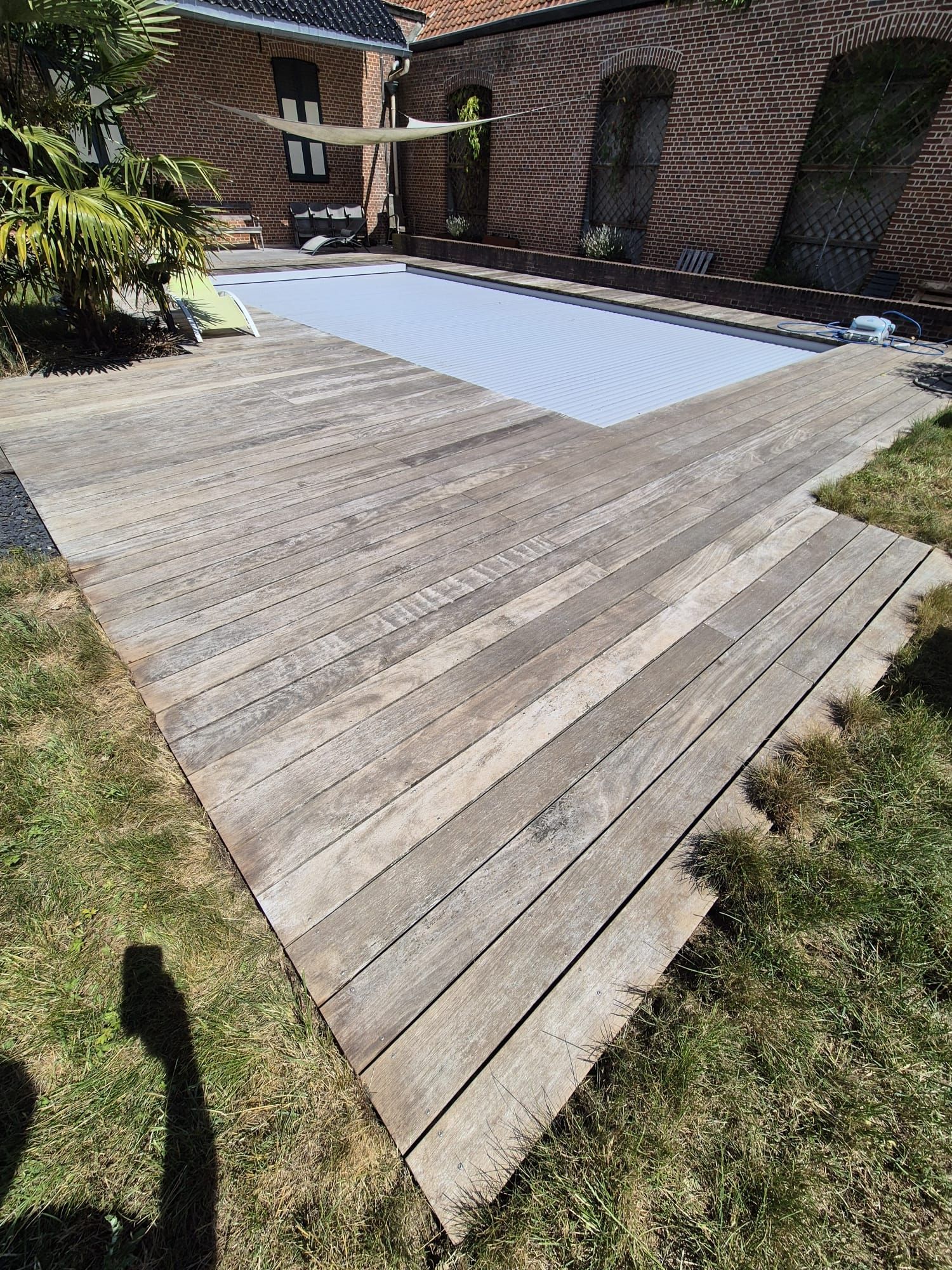 Chemin en briques le long d'un mur de briques et d'herbe, avec des plantes en pot visibles.