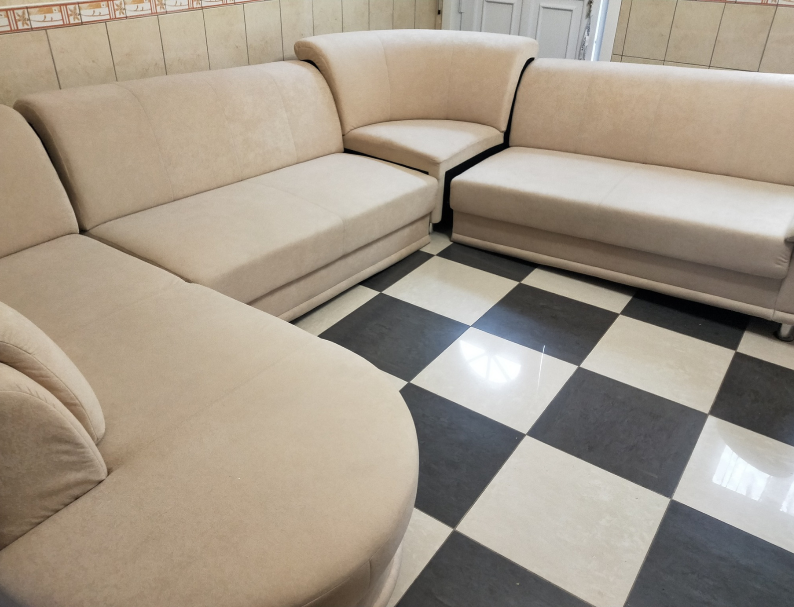 Canapé sectionnel beige dans une pièce avec sol à carreaux noirs et blancs.