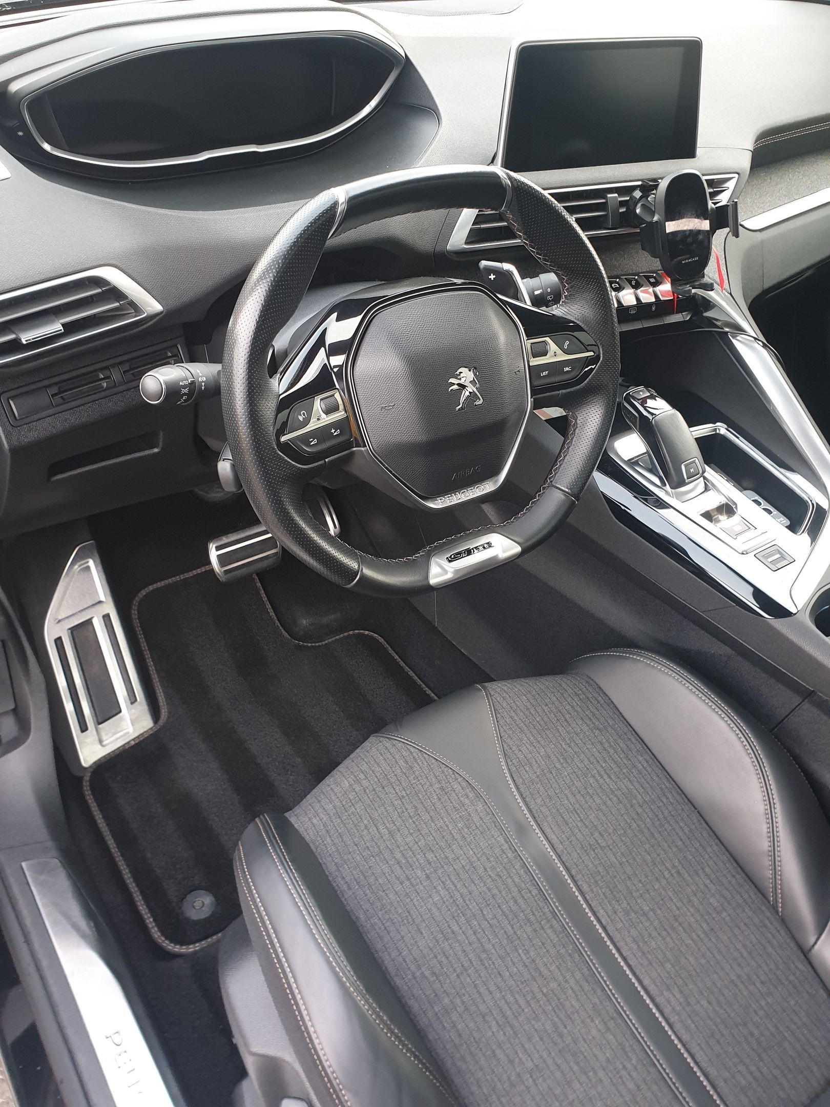 Intérieur d'une voiture Peugeot, montrant le volant, le tableau de bord et le siège conducteur.