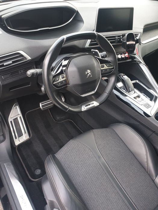 Vue intérieure d'une voiture Peugeot : volant, tableau de bord, sièges noirs et touches argentées.