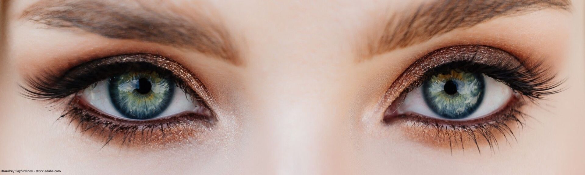 Nahaufnahme von zwei hellblauen Augen mit braunem Lidschatten und dunklen Wimpern.