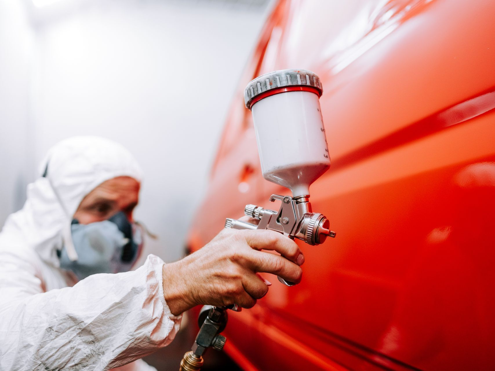 Un homme avec masque et protection repeignant une voiture