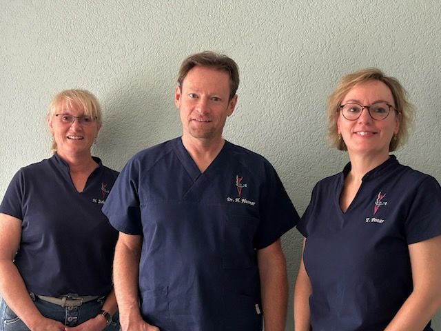 Ein Mann und zwei Frauen in OP-Kleidung posieren für ein Foto