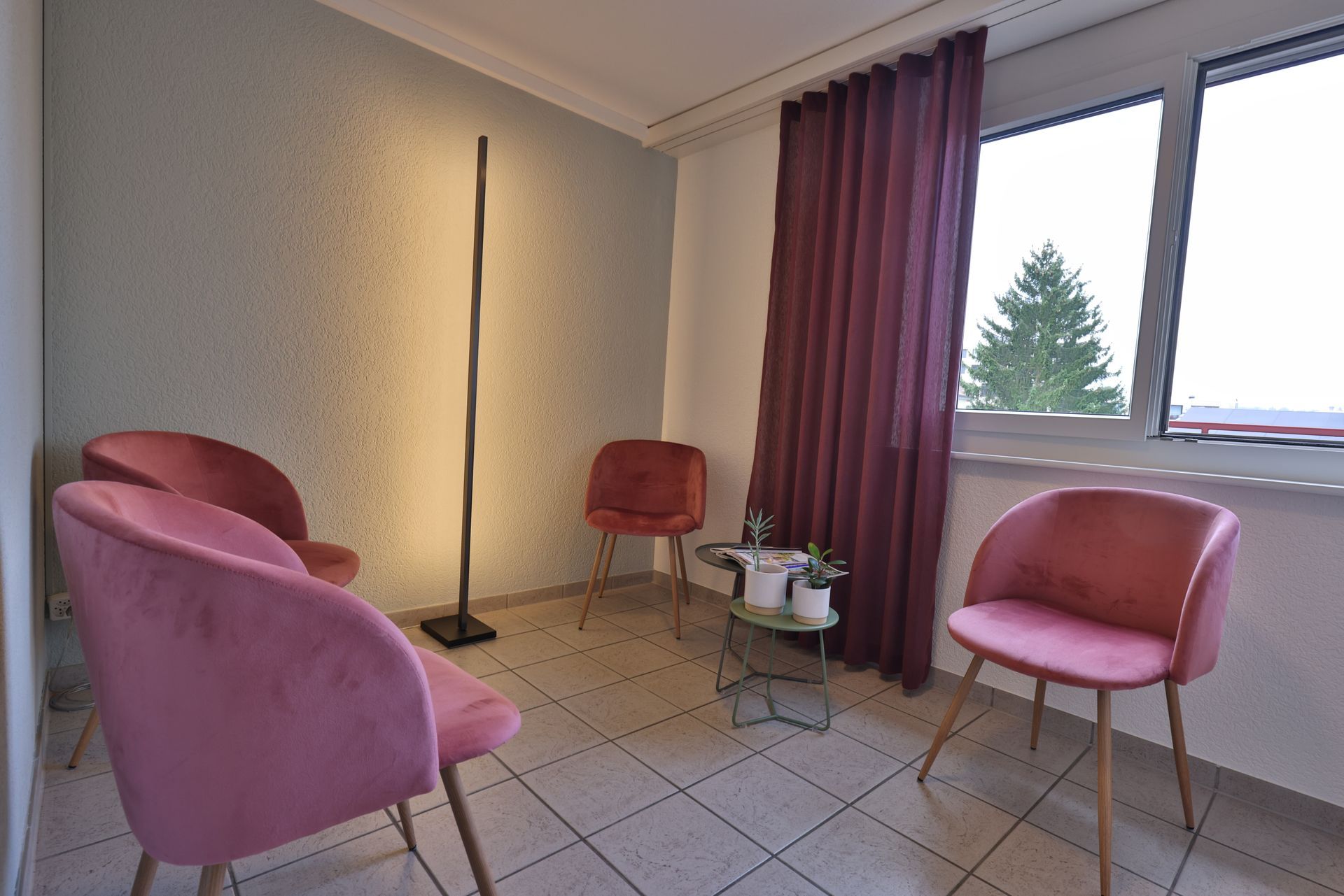 Ein Wartezimmer mit rosa Stühlen, einem Tisch und einem Fenster.