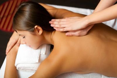 Personne recevant un massage du dos dans un spa, les mains appliquant une pression sur les épaules.
