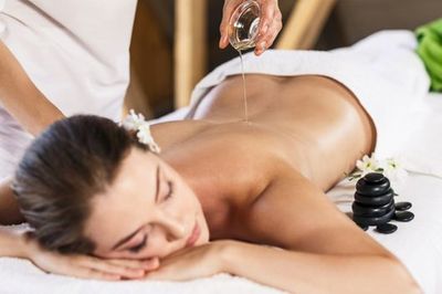 Femme recevant un massage du dos, de l'huile versée, une serviette blanche, des pierres noires, un cadre spa.