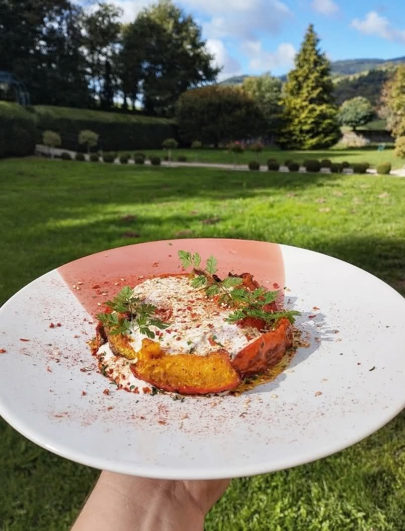 Gros plan sur un plat de courge rôtie servie avec une sauce à la crème et aux herbes, présenté en extérieur sur fond de paysage herbeux pittoresque.
