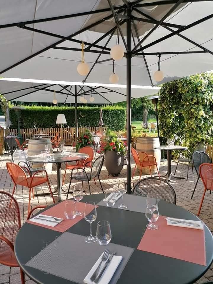 Une terrasse de restaurant en plein air avec des tables rondes, des chaises orange et des parasols blancs, sous un ciel radieux et ensoleillé.