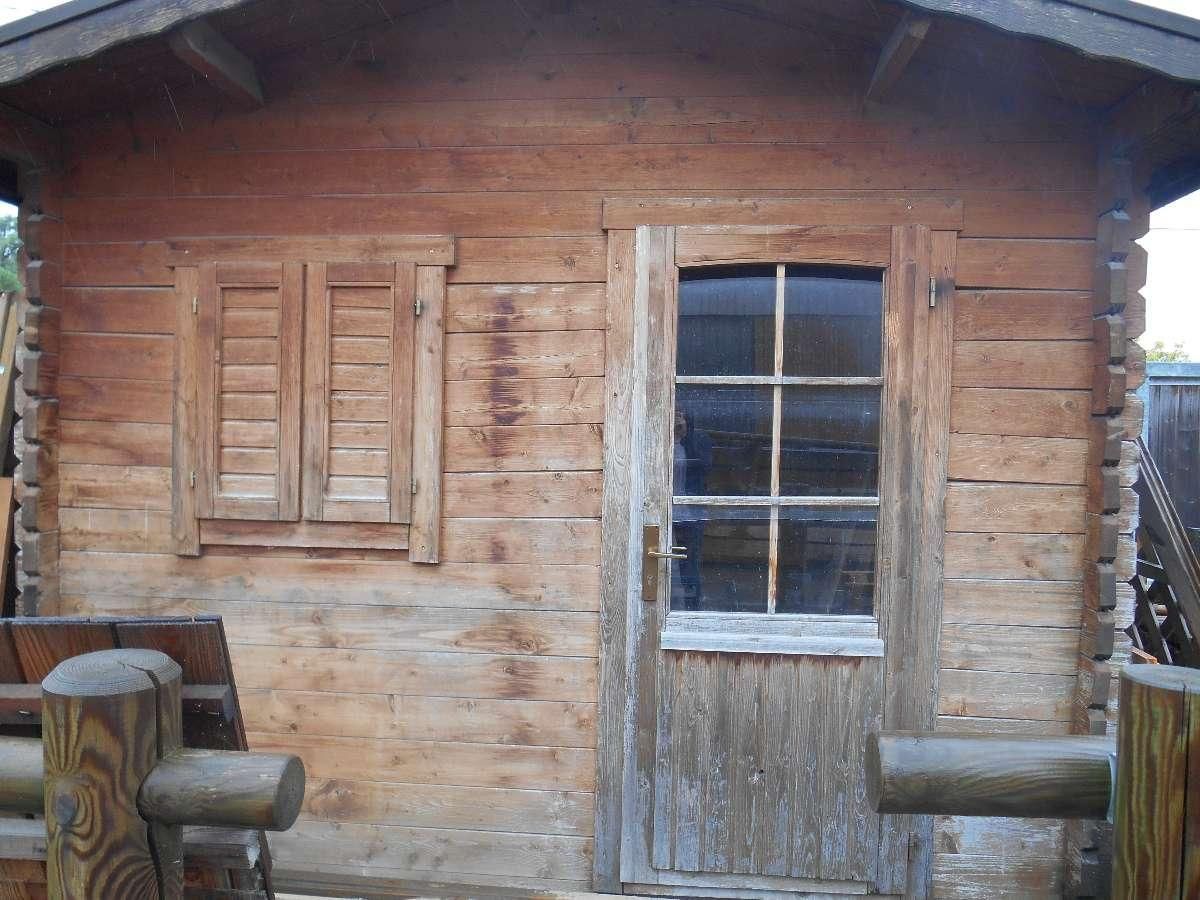 Mur de cabane en bois patiné par le temps, fenêtre à volets, vieille porte et poteaux de porche rustiques.
