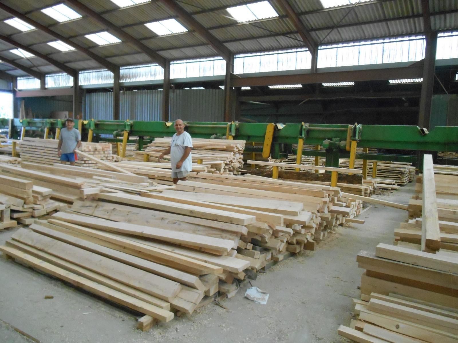 Des ouvriers trient des piles de planches et de poutres de bois coupées dans un entrepôt de bois.