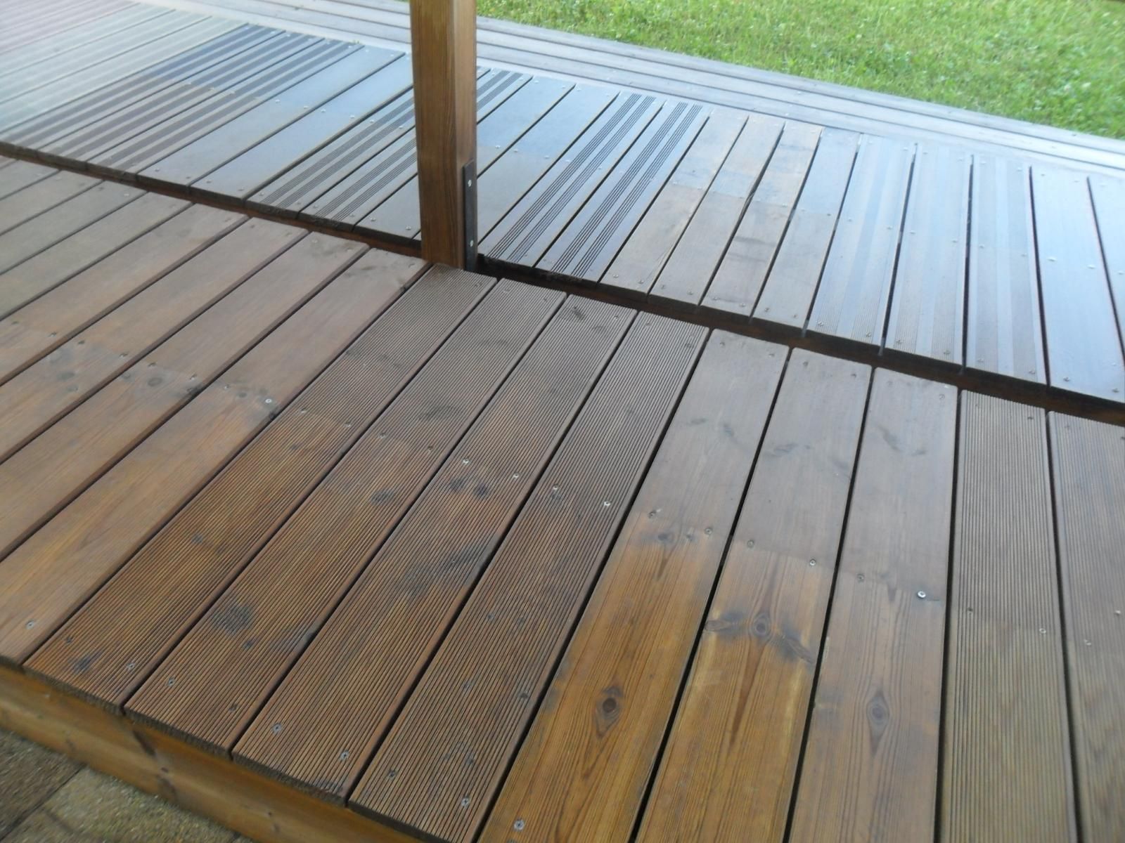 Terrasse en bois avec rambarde en verre ou en métal, donnant sur la pelouse extérieure.