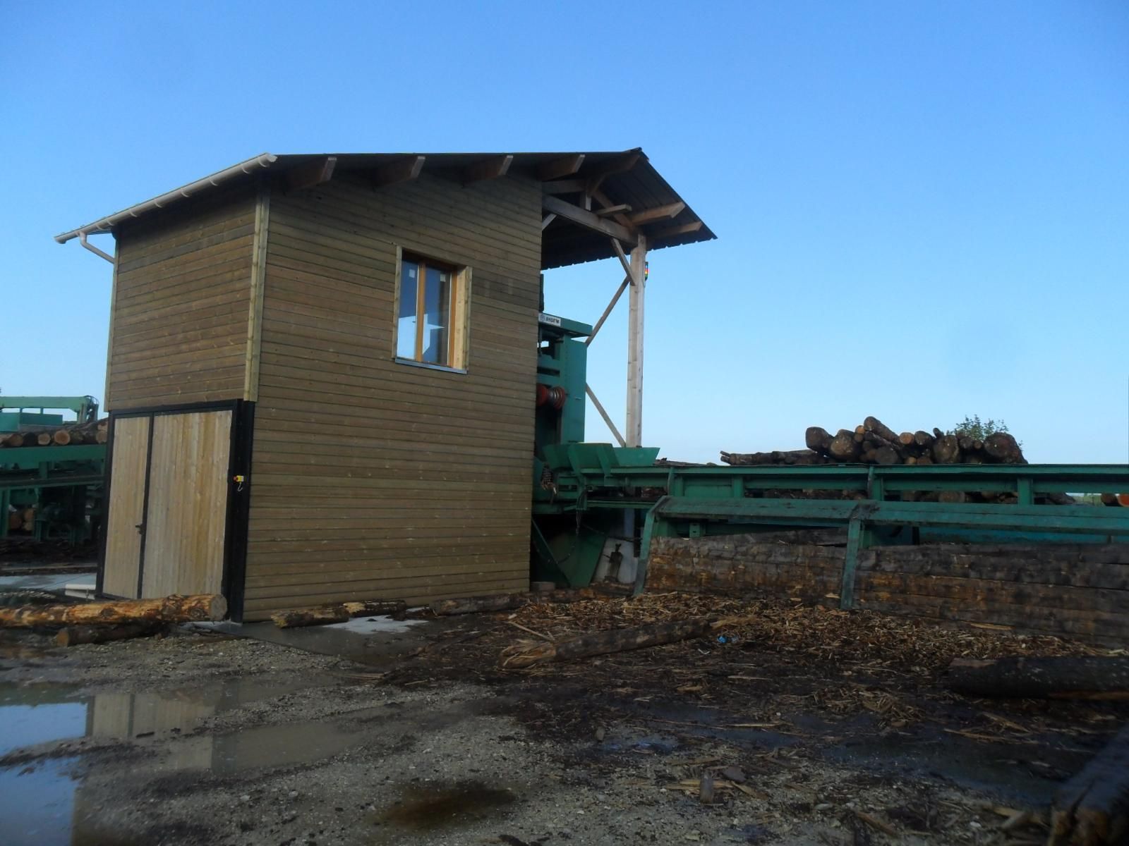 Petit hangar en bois à côté de machines agricoles vertes dans une cour ouverte sous un ciel bleu clair
