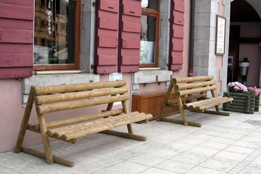Deux bancs en bois sur un trottoir devant un bâtiment rouge avec des fenêtres et des pots de fleurs