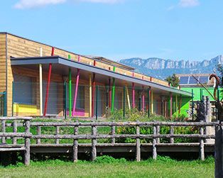 Bâtiment coloré avec des poteaux arc-en-ciel, pelouse clôturée et montagnes en arrière-plan