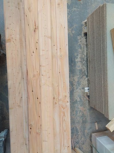 Des planches et des panneaux de bois empilés contre un mur en béton brut dans un atelier ou un chantier.