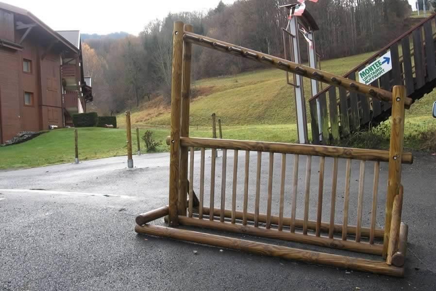 Un portail métallique rouillé bloque une route à côté d'un bâtiment en briques et d'une colline herbeuse.