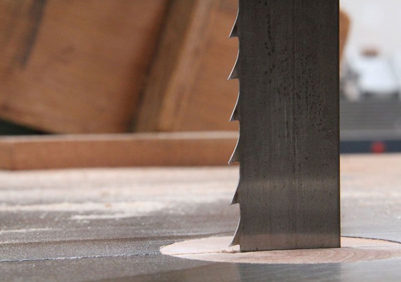 Gros plan d'une lame de scie à ruban coupant du bois sur une table d'atelier