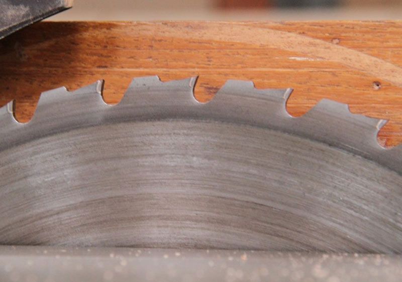 Gros plan sur une lame de scie circulaire coupant du bois, avec des dents argentées acérées et de la sciure de bois sur une surface en bois.