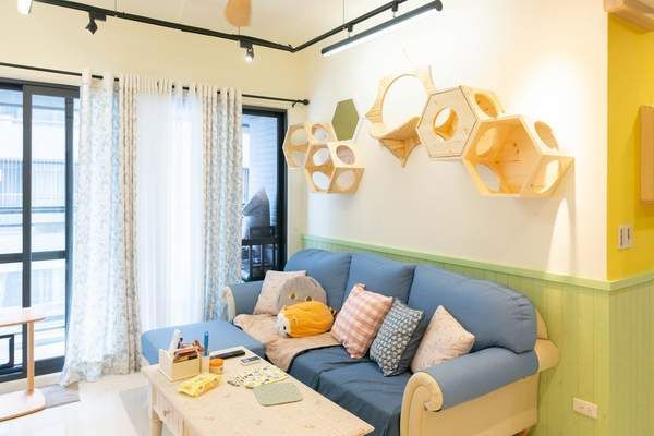 Salon aux tons pastel lumineux avec canapé bleu, étagères murales hexagonales et grandes fenêtres avec rideaux.