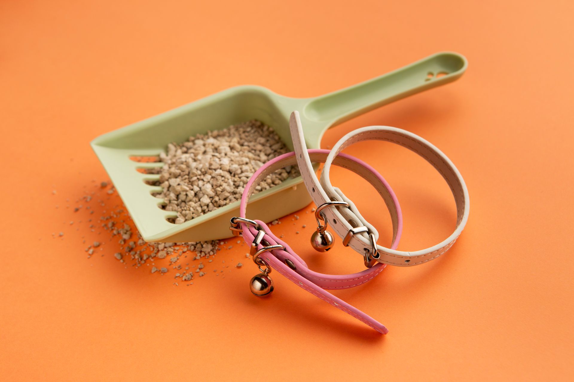 Trois colliers pour chats avec des clochettes et une pelle à litière sur fond orange.