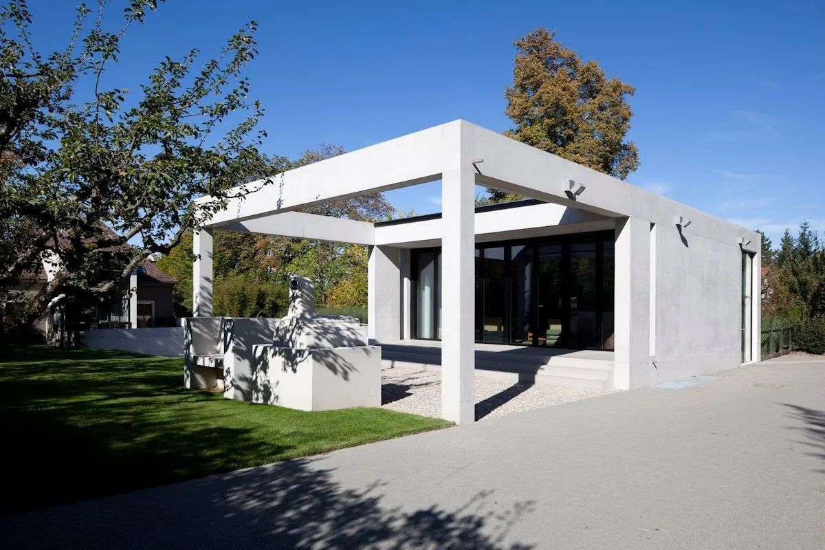 Une maison blanche avec beaucoup de fenêtres est entourée d'arbres et d'herbe.