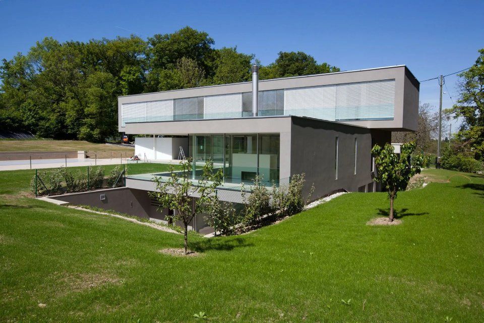 Une grande maison avec beaucoup de fenêtres se trouve au milieu d'un champ verdoyant.