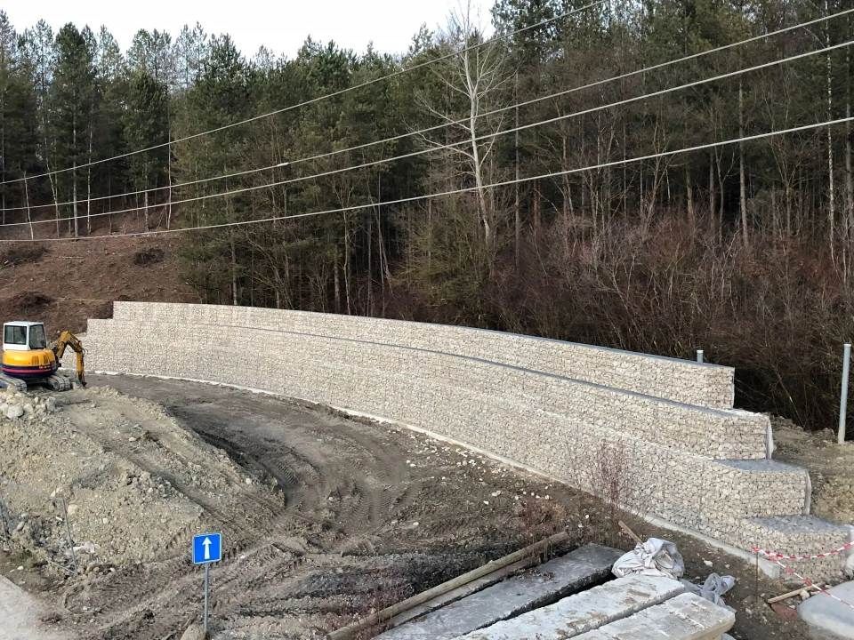 Un grand mur de pierre est en cours de construction à côté d'une route.