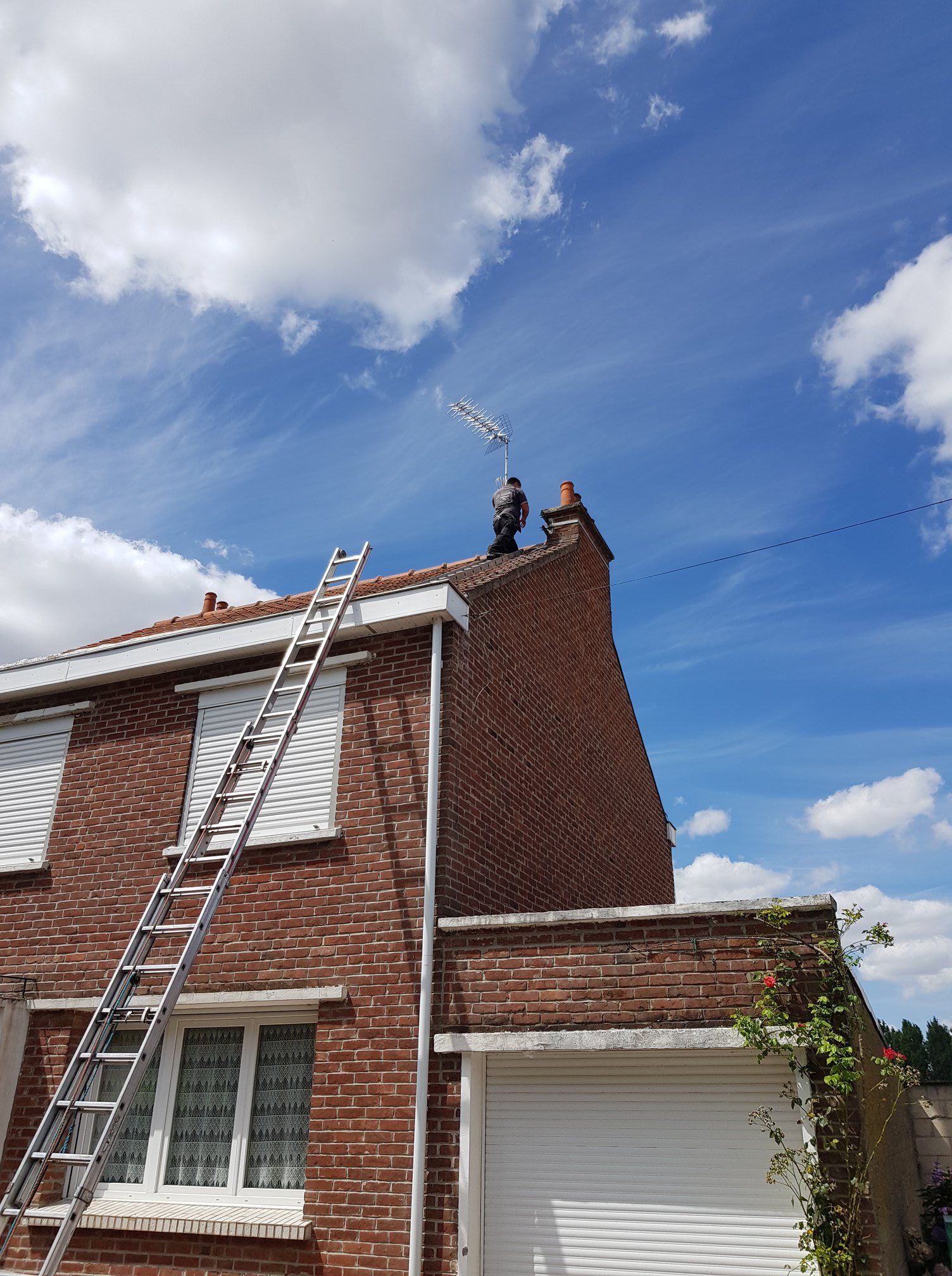 Maison en briques avec deux échelles appuyées contre le toit sous un ciel bleu parsemé de nuages.