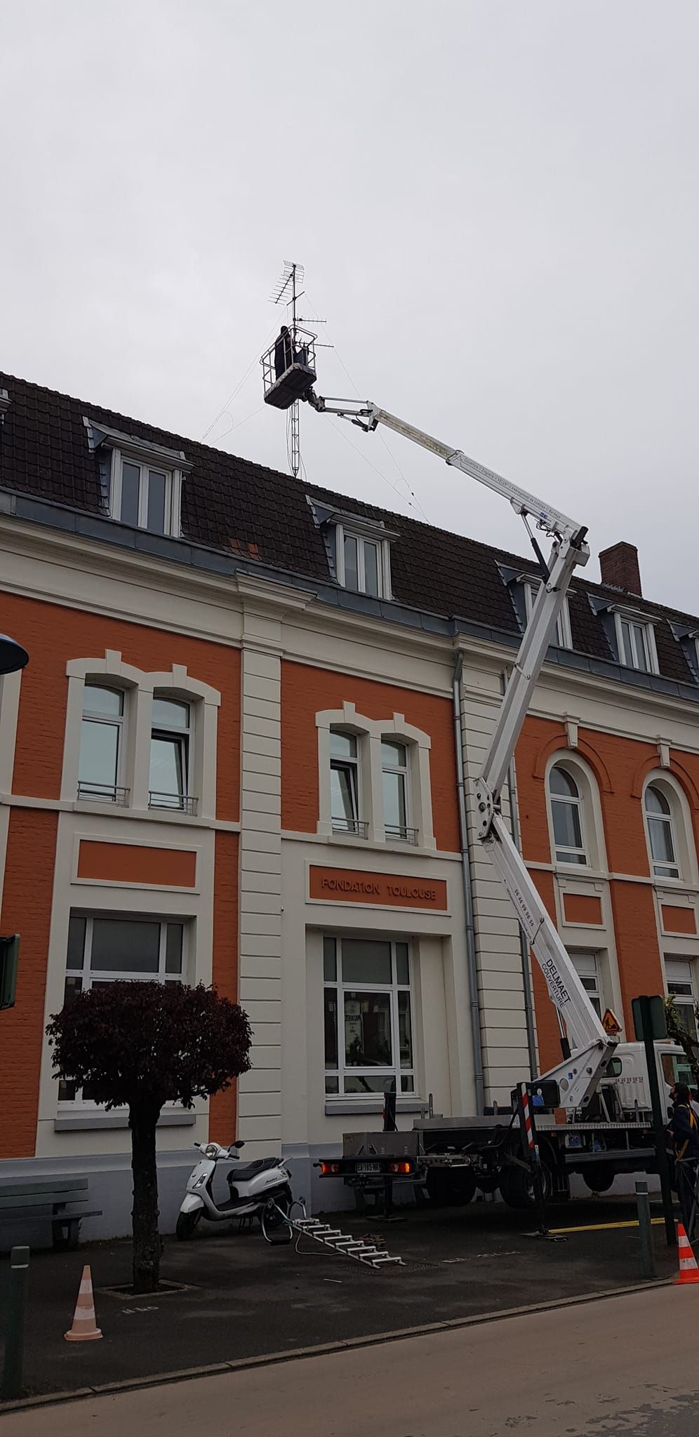 Vue de rue montrant des immeubles en briques rouges aux boiseries blanches, des voitures garées et une grue.