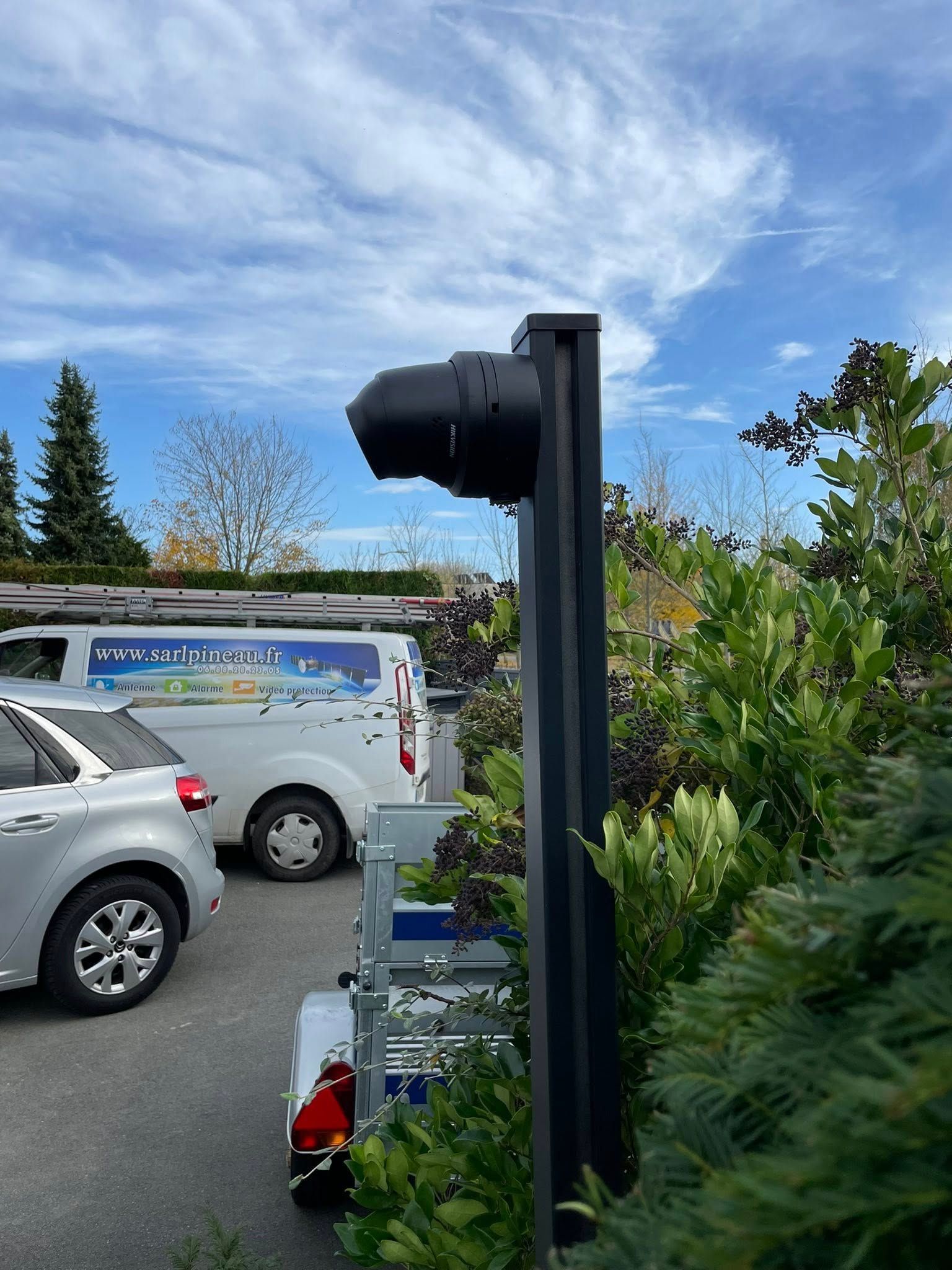 Un parking avec des voitures, une camionnette blanche et un grand poteau noir se détachant sur un ciel bleu.