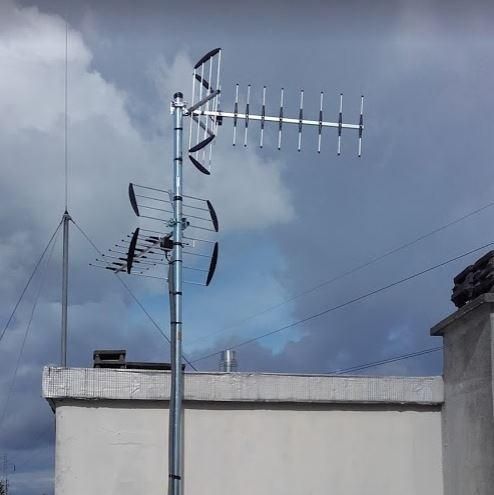 Antennes de télévision sur le toit d'un bâtiment blanc, se détachant sur un ciel gris nuageux.